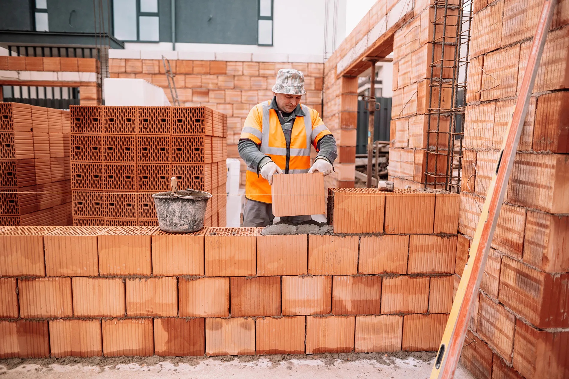 A man in a yellow vest is building a brick wall.